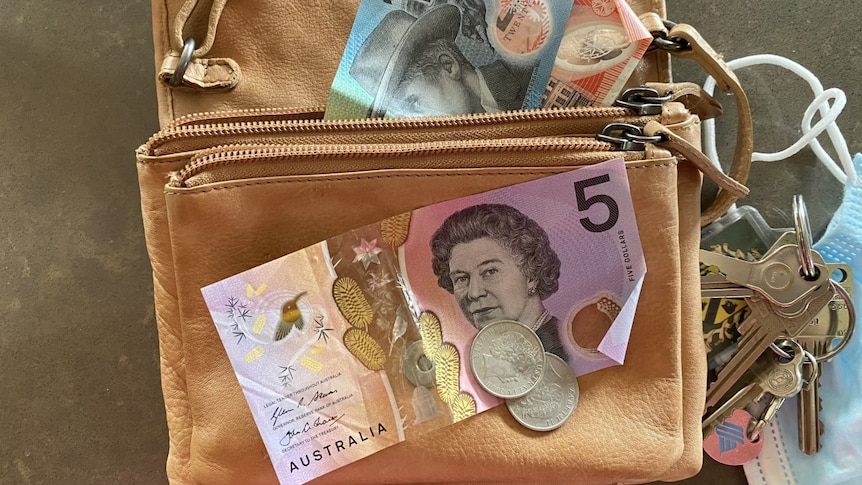 Close-up of Australian currency on leather handbag with keys and face mask to the right
