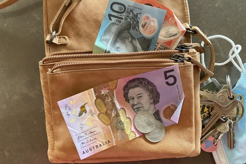 Close-up of Australian currency on leather handbag with keys and face mask to the right