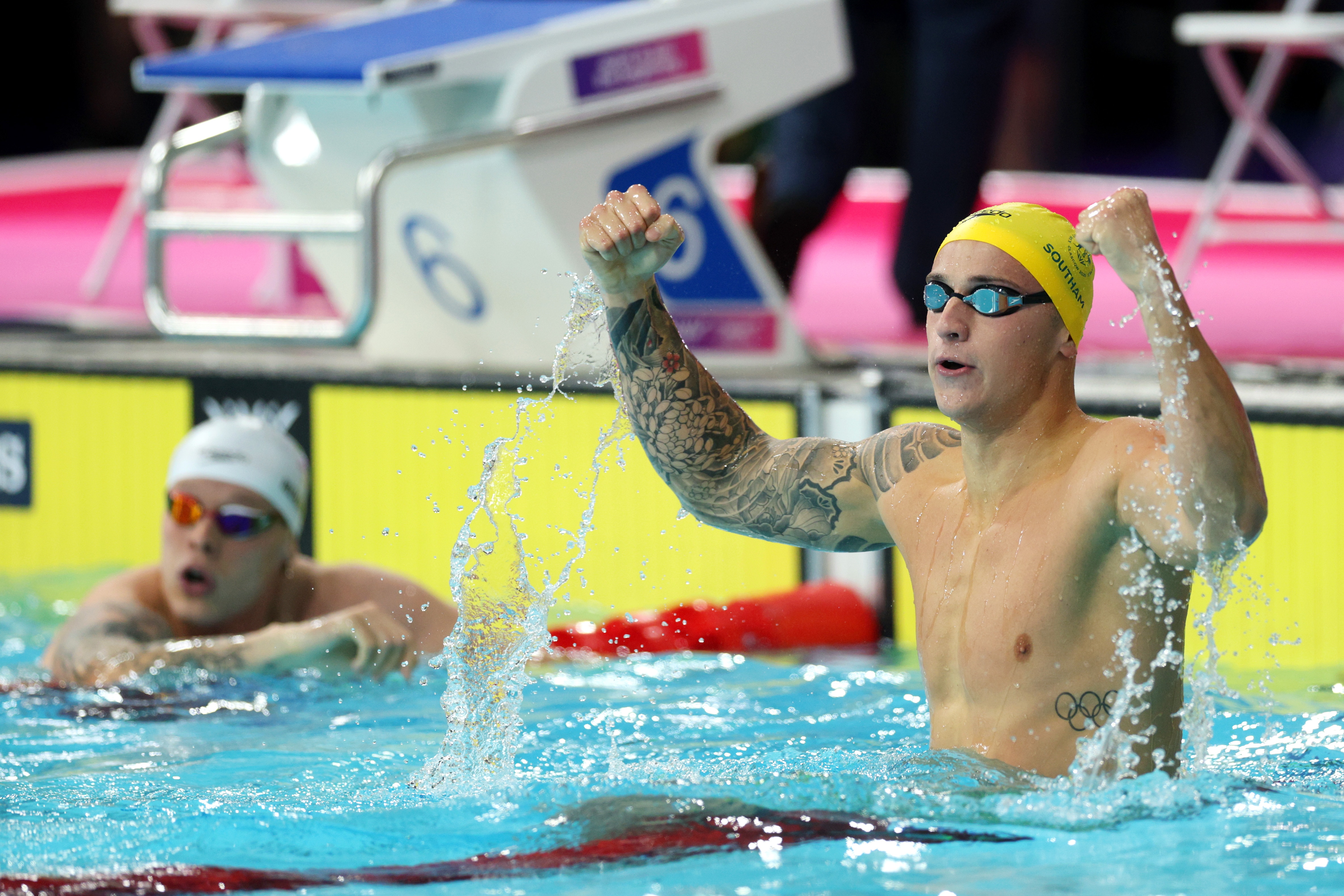 An Australian swimmer stands in the pool with both fists pumped as he celebrates a gold medal.