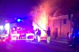 Fire fighters standing in front of a fire truck hosing a large fire.