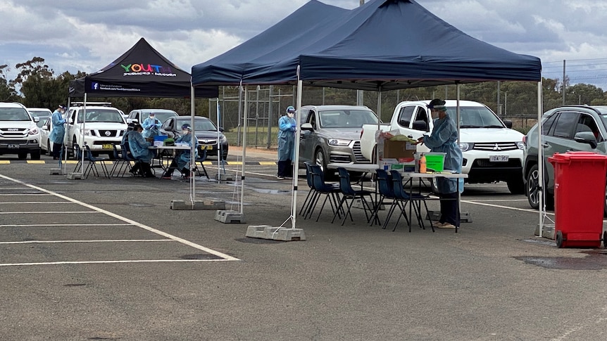 A group of people in protective clothing swab people in their vehicles.