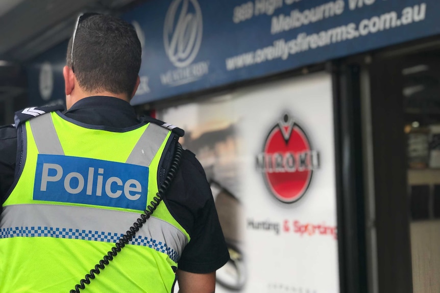 A rear shot of a police officer's fluro vest, with a police sign, outside a gun store.