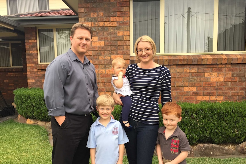 Family of mum, dad, two boys and a baby girl stand out front of a home