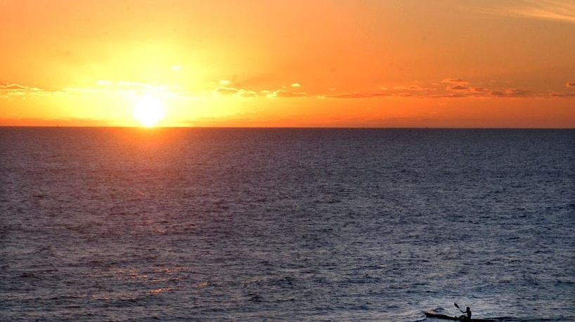 A man paddles his kayak at sunset