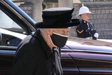 A close-up of the Queen shows her n black mourning attire, with a black hat and face mask. 