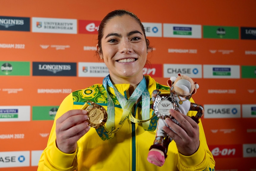 A female athlete wearing yellow and green holds up two medals
