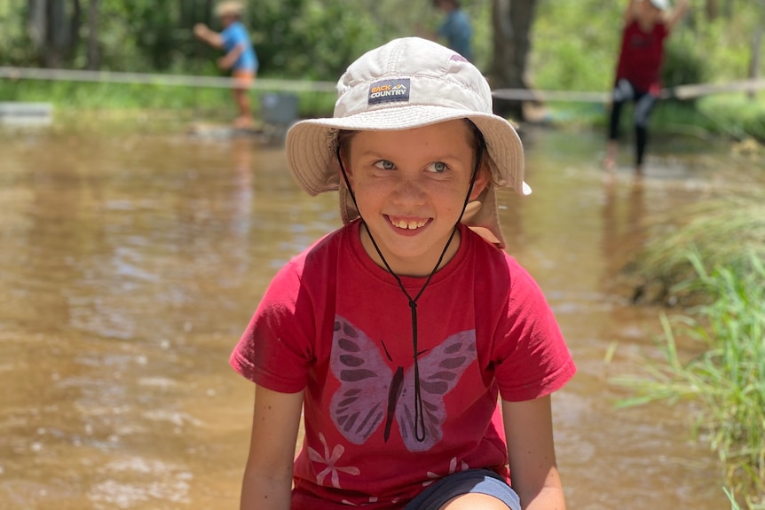 young boy crouching down in front of a dam 