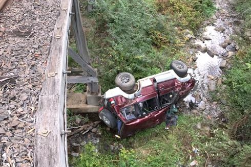 A car laying in a creek bed with a bridge in the foreground.
