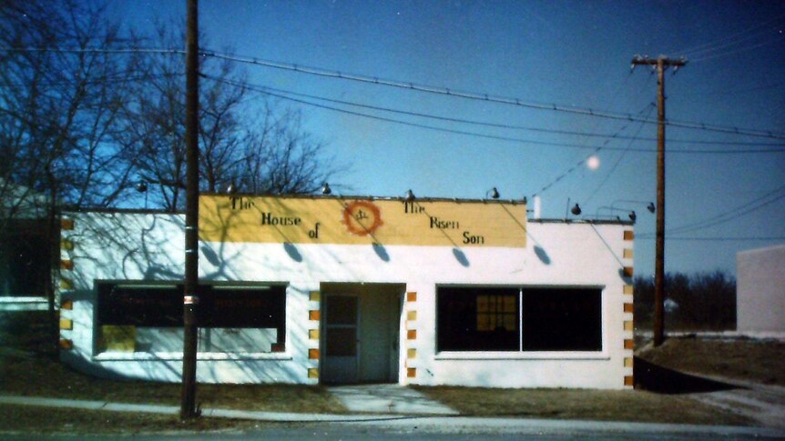 A white house sits behind a road underneath a blue sky and power poles.