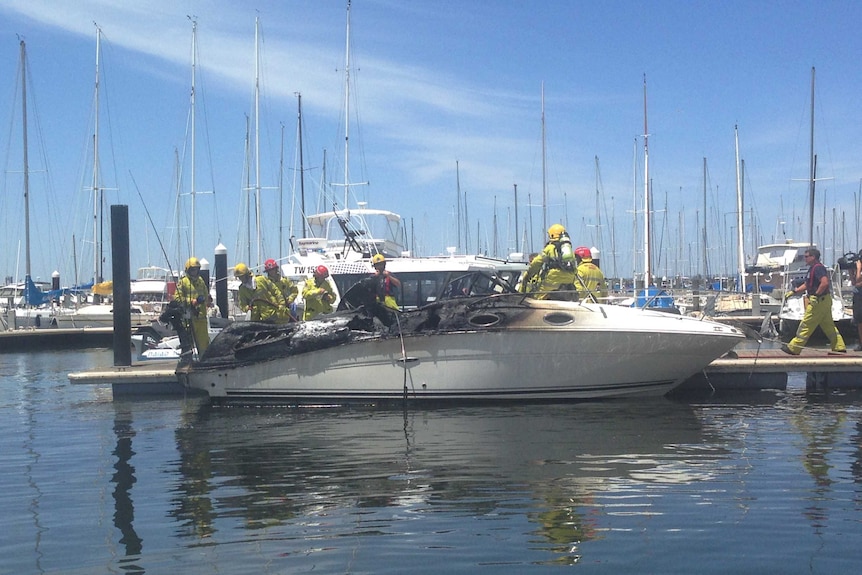 A boat that was damaged by fire sits moored in Matilda Bay with fire crews assessing the vessel.