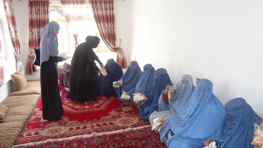 Veiled women seated on rugs in a room sharing vegetable seeds