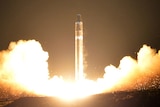 Smoke and flames come from the bottom of a cylindrical intercontinental ballistic rocket as it launched at night.