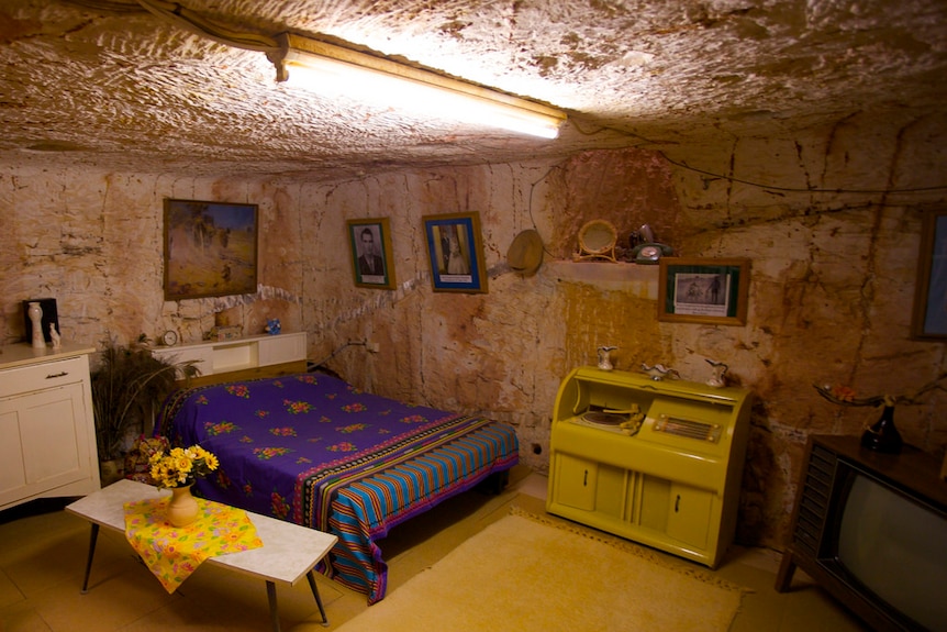 An underground bedroom in Coober Pedy with brown coloured walls made of rock and a bed.