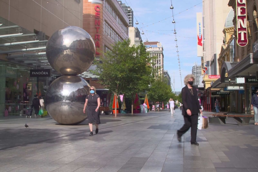 People walking in a pedestrian mall with a sculpture of two balls on top of each other