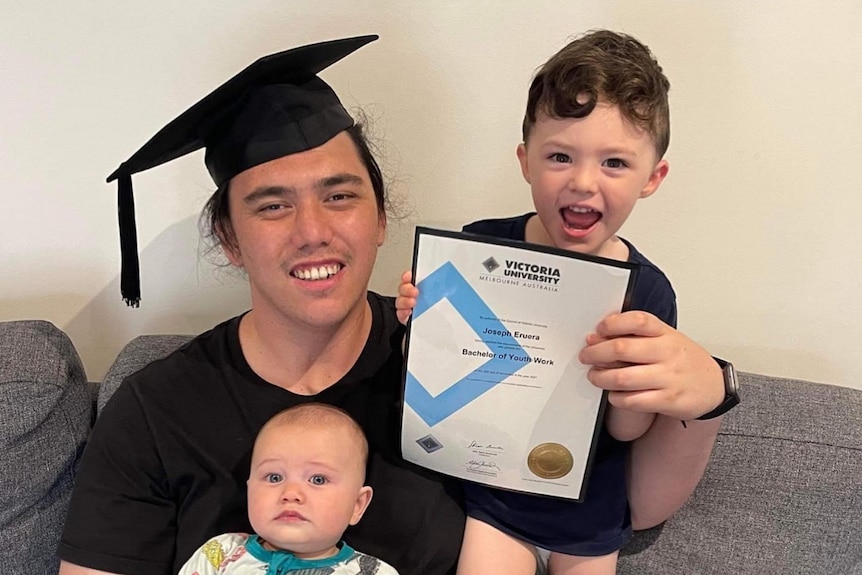 a young man wearing an academic cap holds his bachelor's certificate and his two children