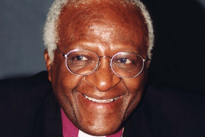 A close up photo of Desmond Tutu smiling in a clerical collar and black jacket