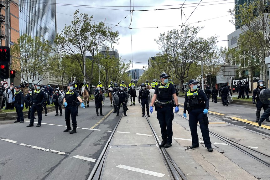Large number of police stand on tram lines and middle of street in Melbourne CBD.