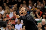A coach dressed in a dark suit yells with his hand outstretched during a game.