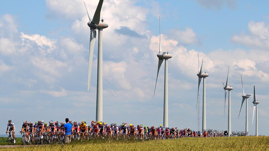 The peloton passes by windmills during the Tour de France.