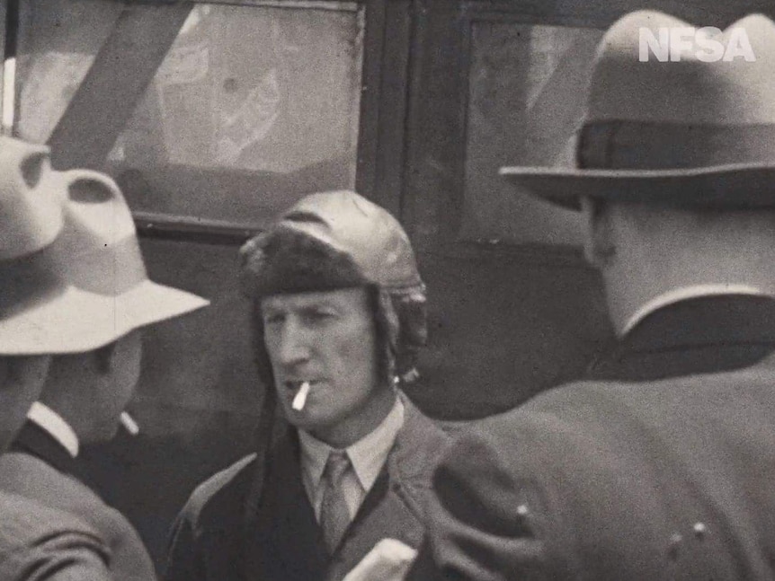 Kingsford Smith smokes a cigarette next to the plane.