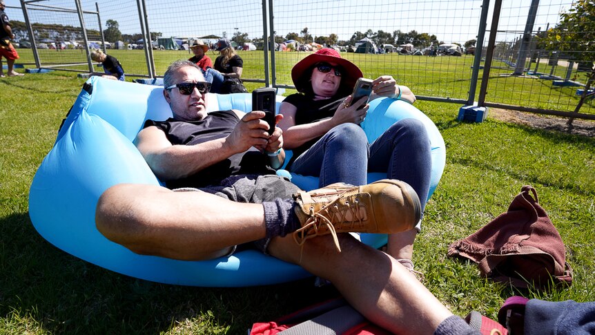 A couple of punters from Melbourne sit on an inflatable couch looking at their phone while waiting for gates to open.