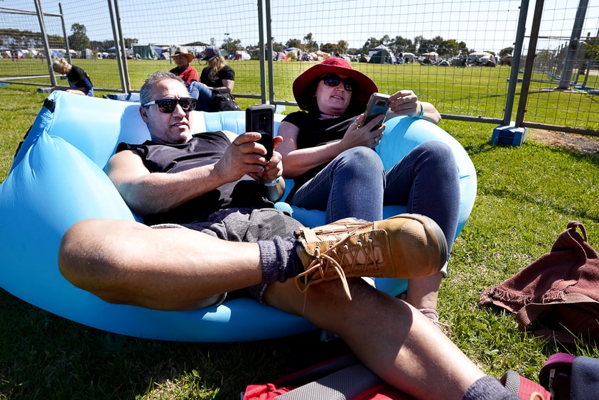 A couple of punters from Melbourne sit on an inflatable couch looking at their phone while waiting for gates to open.