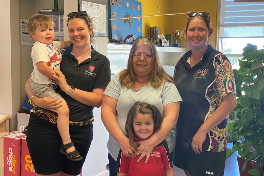 Three women stand indoors with two young children. Everyone is smiling.