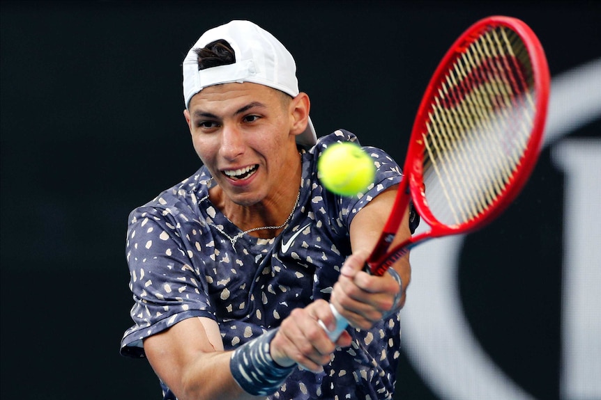 A male tennis player watches the ball as he plays a double-handed backhand at the Australian Open.