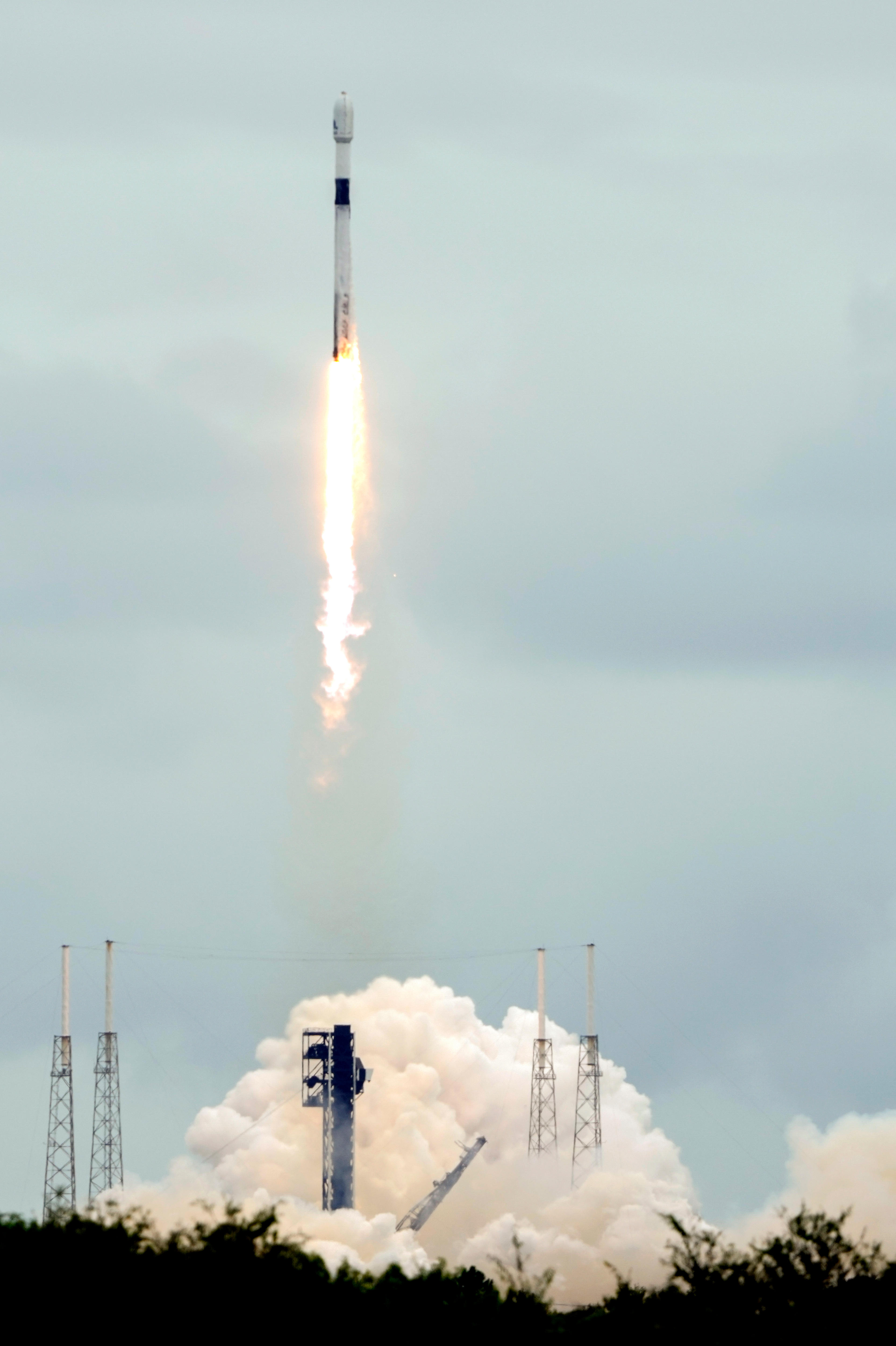 A rocket in the sky with a trail of fire behind it and its support structure on the ground collapsing.