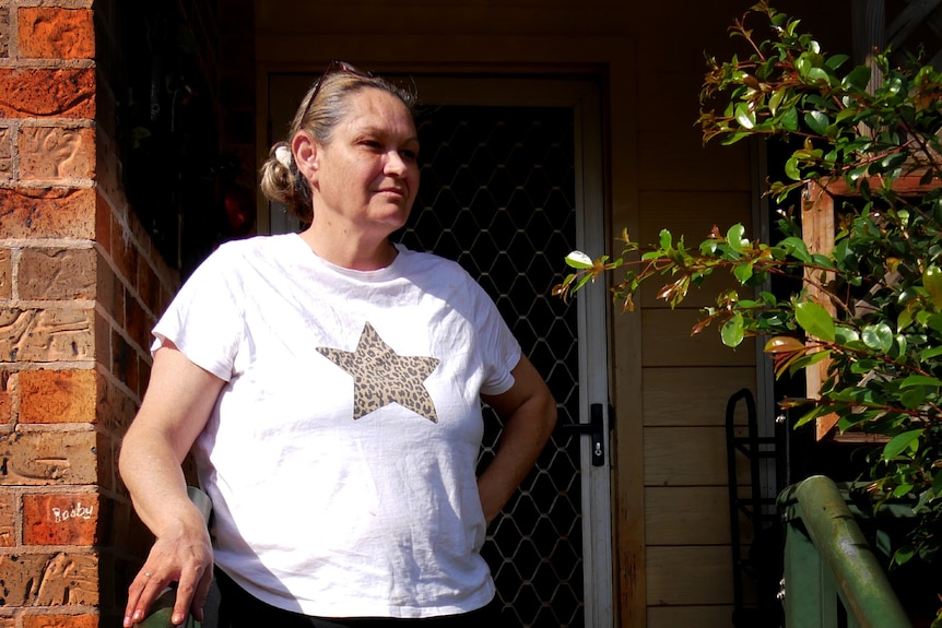 A woman in a white t-shirt with a gold star standing on steps in front of a brick house