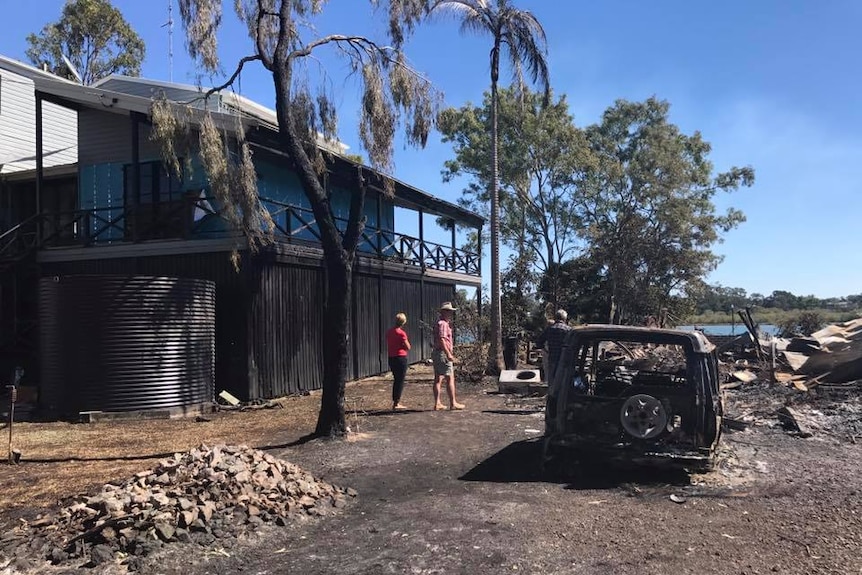 A two-storey house with fire damage, car burnt out, tin and remnants of other burnt items.