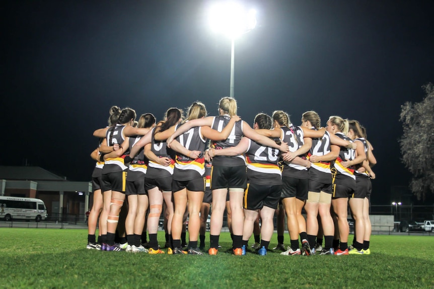 Bendigo Thunder women's AFL team in a team huddle under a floodlight