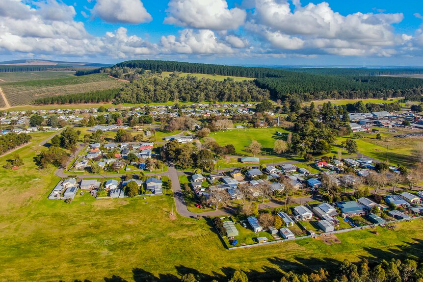 An aerial photo of a small town surrounded by lush green paddocks and forest.