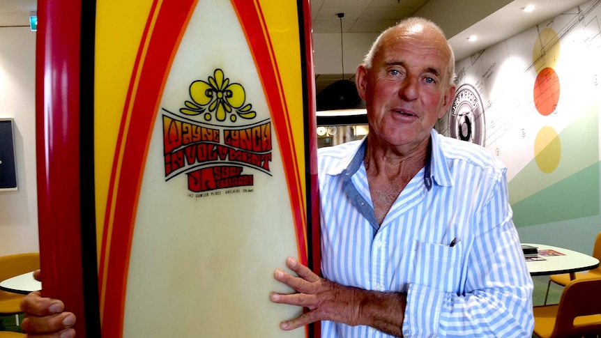 A man stands smiling next to a red yellow and black surfboard