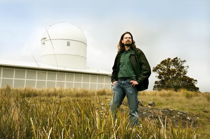 man with long hair in field beside observatory.
