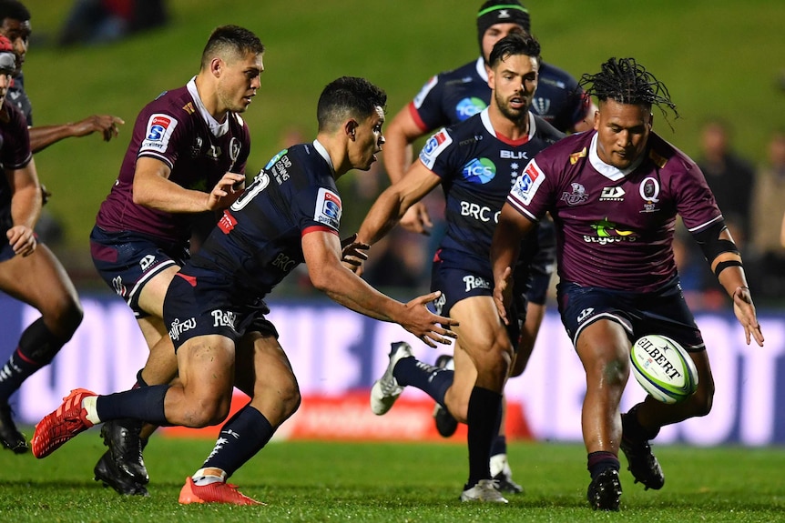 A Melbourne Rebels player and a Queensland Reds opponent run towards the ball in a Super Rugby AU match in Sydney.