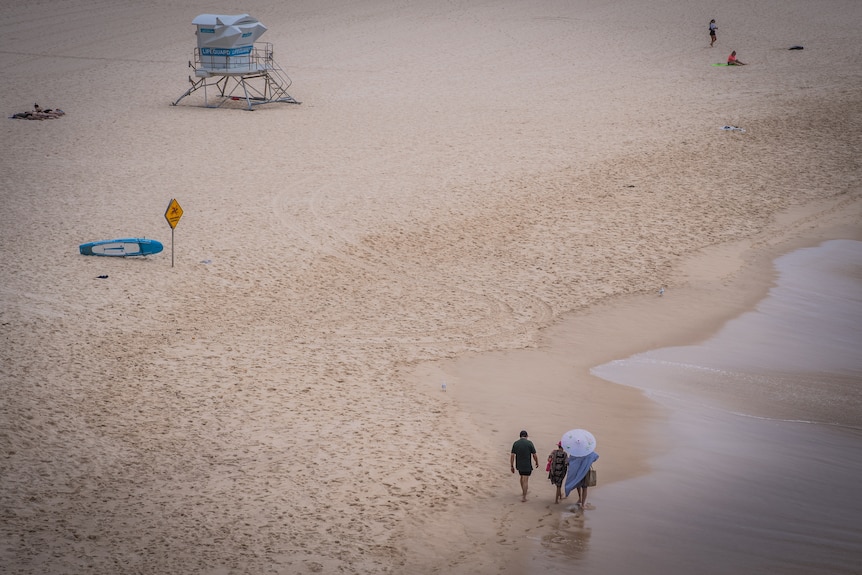 Three peopl walking along Bondi Beach