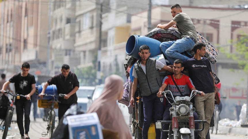 Four men on a three-wheeled motorbike and a trailer, carrying containers and mattresses.