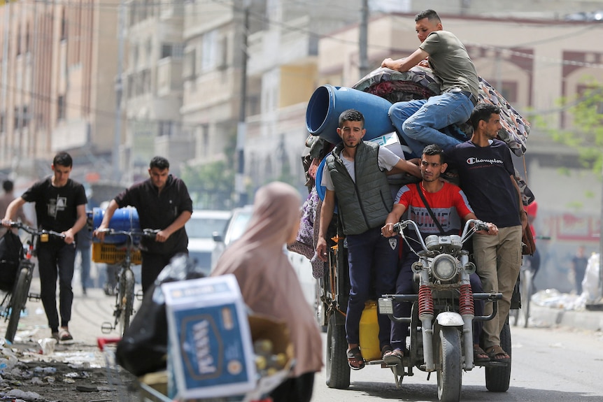 Four men on a three-wheeled motorbike and a trailer, carrying containers and mattresses.