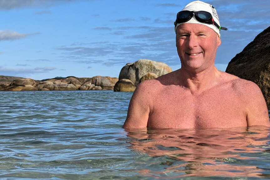 A man in goggle chest deep in ocean