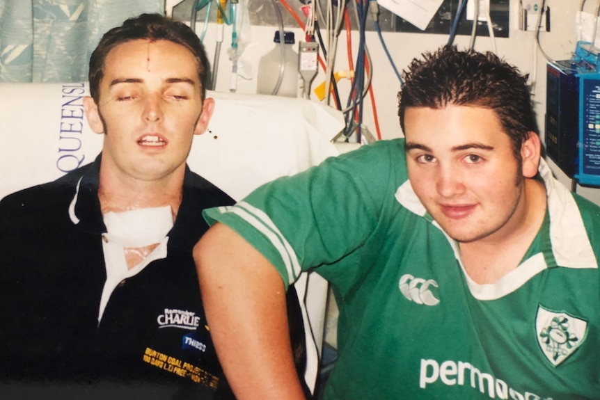 a man lays in a hospital bed with another man by his side