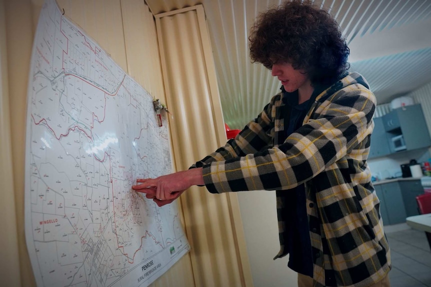 A teenager stands and points to a map of the town of Penrose. He is standing in the kitchen of an R-F-S shed