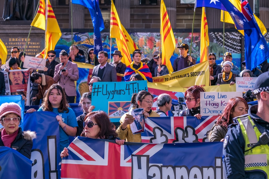 A group of protesters stand in front of the neoclassical State Library of Victoria holding banners and Australian flags.