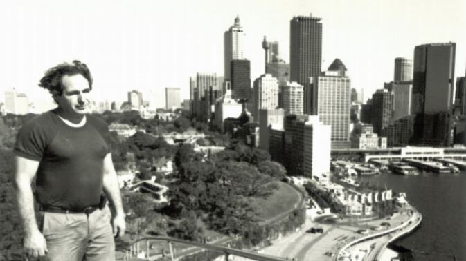 Black and white photo of Steve Tsoukalas standing on the Sydney Opera House sails