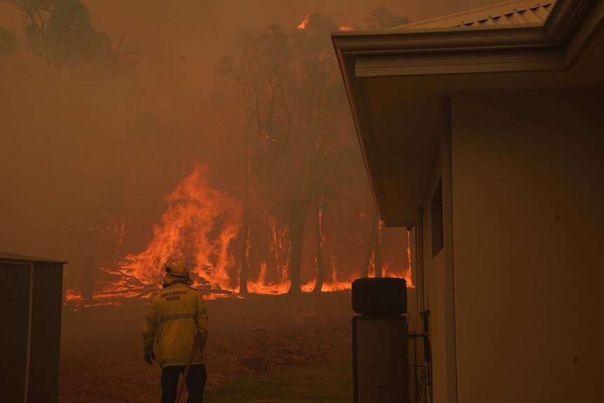 A firefighter battles a wall of flames while defending a property