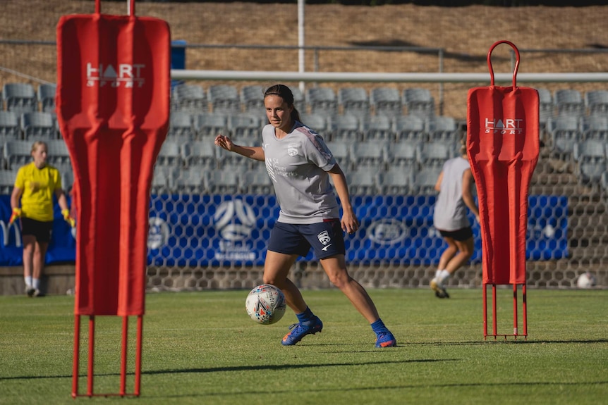 A female football player goes to kick a ball at training.