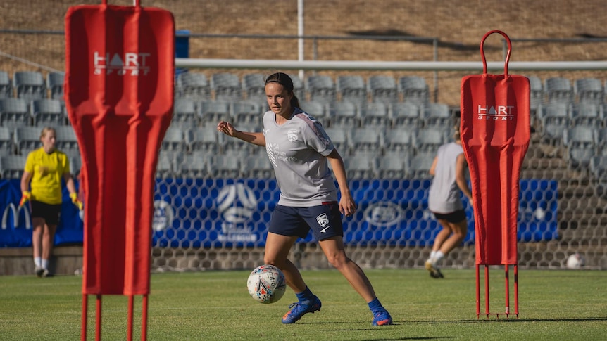 A female football player goes to kick a ball at training.