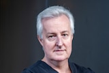 grey haired man with arms crossed wearing blue medical scrubs