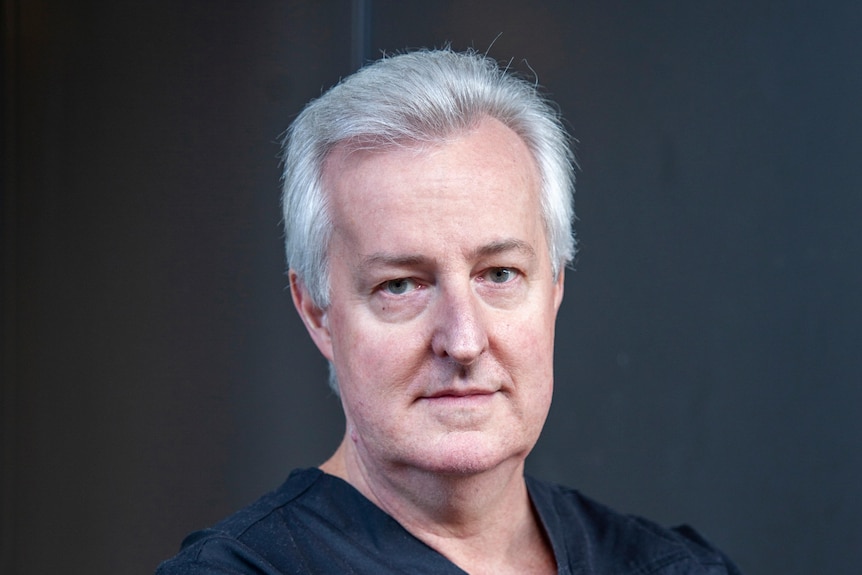 grey haired man with arms crossed wearing blue medical scrubs
