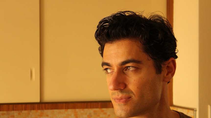 A man with dark hair and brown eyes looks to his right in a kitchen